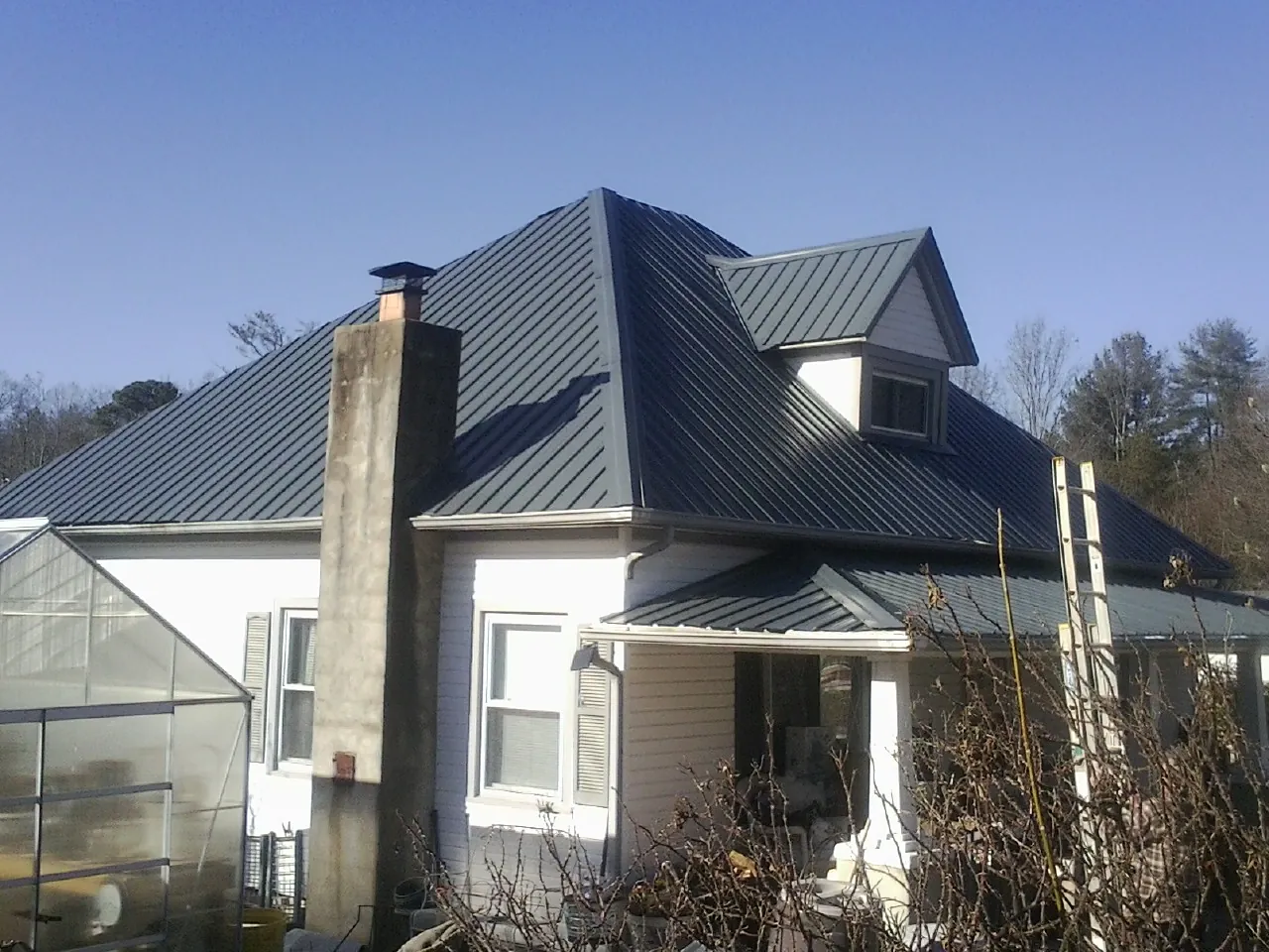 Dark blue standing seam metal roof on a white farmhouse with dormer — Slate & Tile Roof Repair by Roofing Brothers in Conyngham