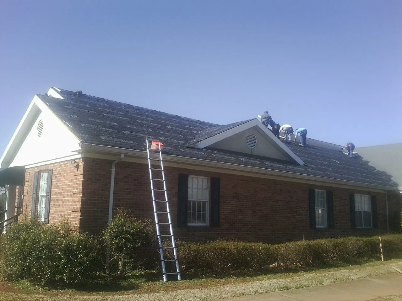 Crew tearing shingles off a brick ranch roof with a ladder set — Emergency Roof Repair work by our crew in Conyngham