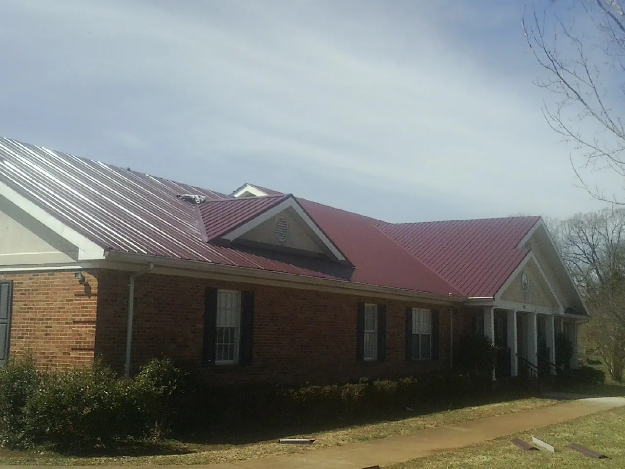 Red metal roof with gabled entries on a long brick building, from a Hail Damage Roof Repair job in Conyngham