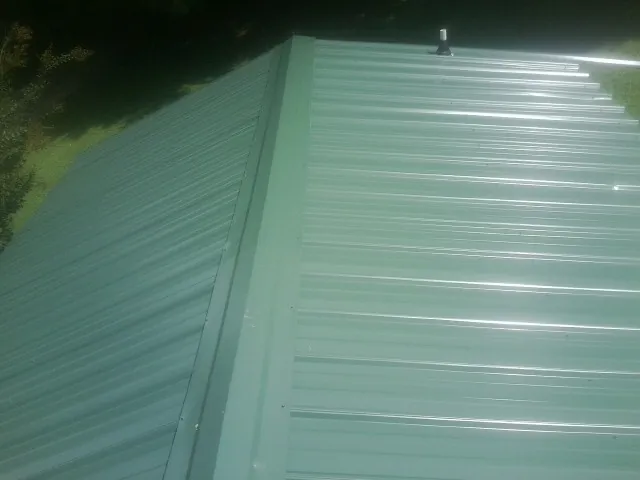 New green metal panels meeting at the ridge of a roof — Flat Roof Repair work by our crew in Conyngham