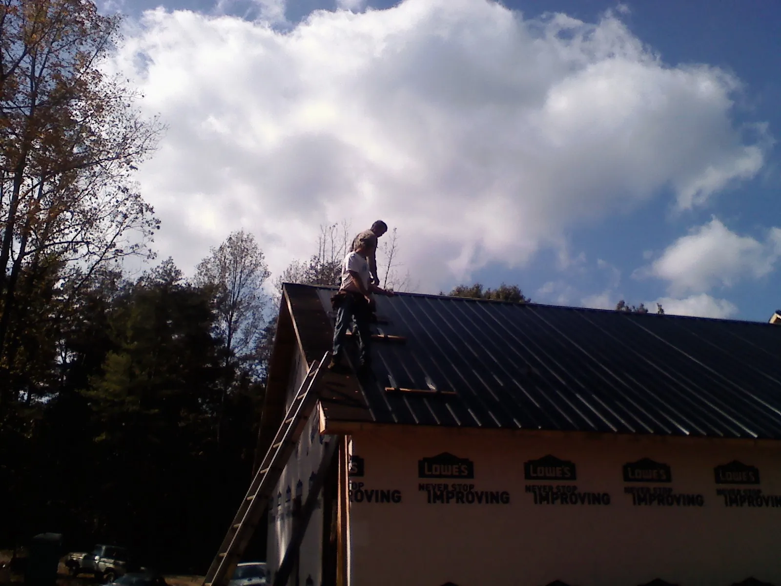 Roofer fastening dark metal panels high against a cloudy sky, from a Roof Inspection job in Conyngham