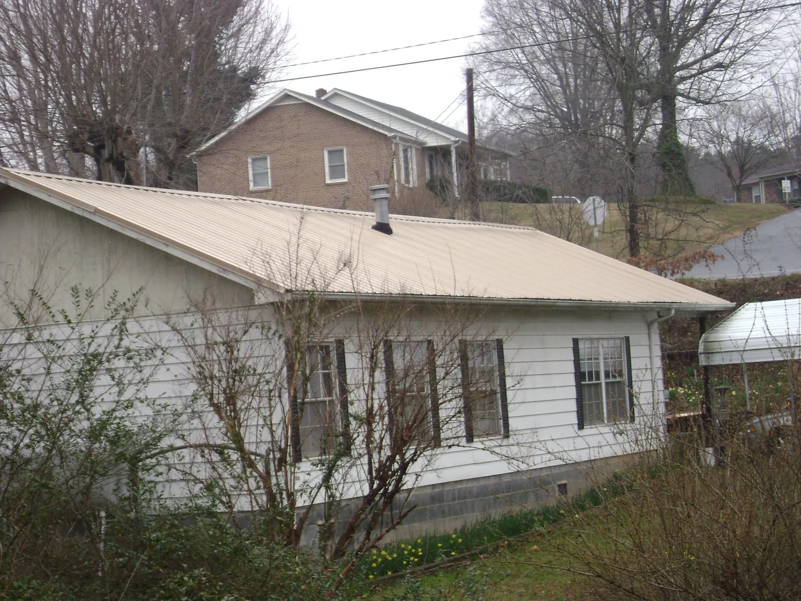 Tan metal roof on a white sided house set into a hillside — Commercial Roofing by Roofing Brothers in Conyngham